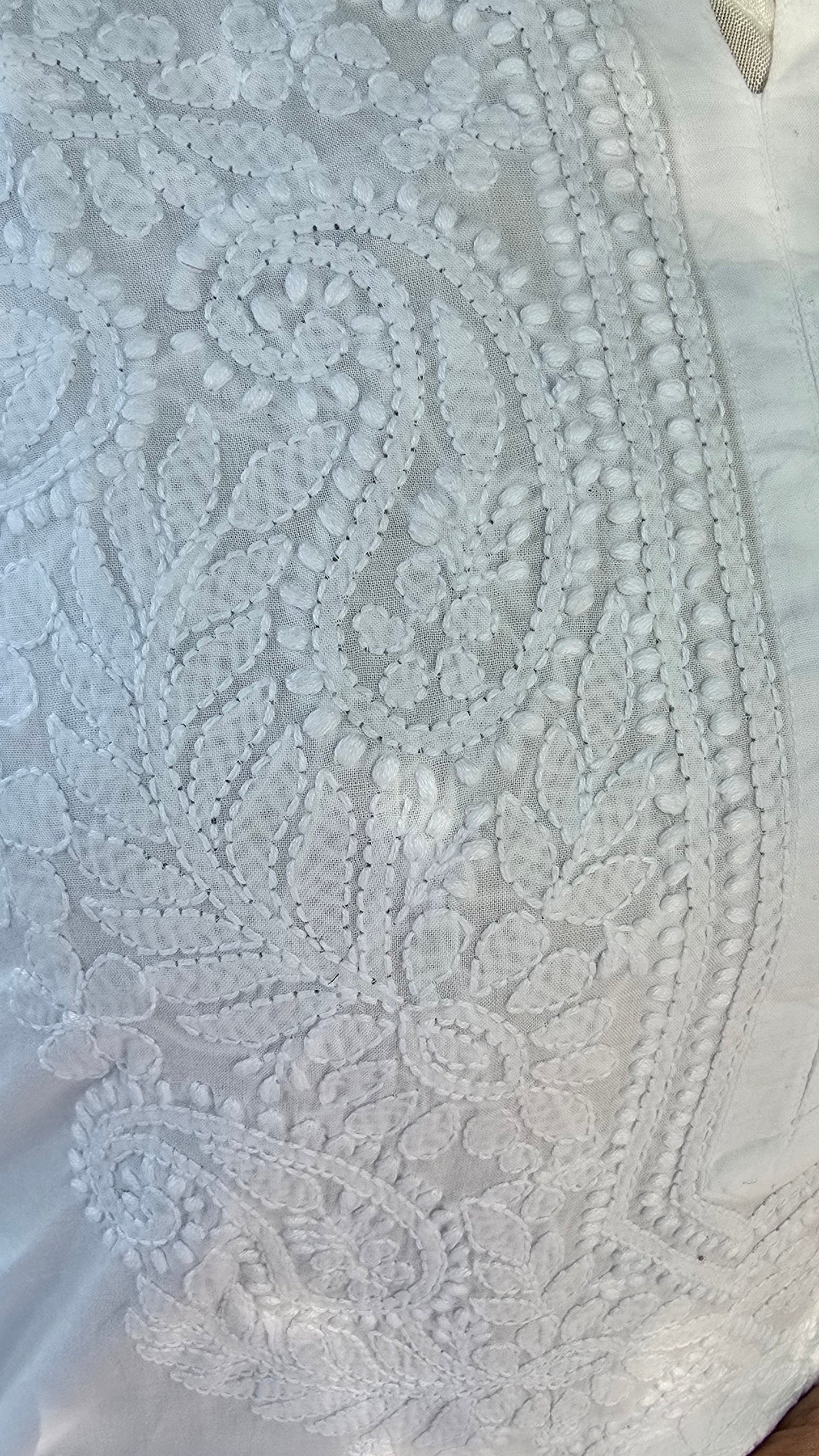 Close-up of white intricate chikankari held by a hand.